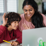 A mother and young son wave to a laptop screen while engaging in online learning