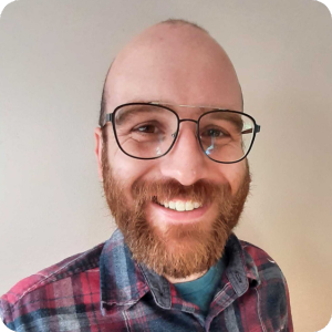 Man with facial hair smiling with glasses wearing a red plaid shirt