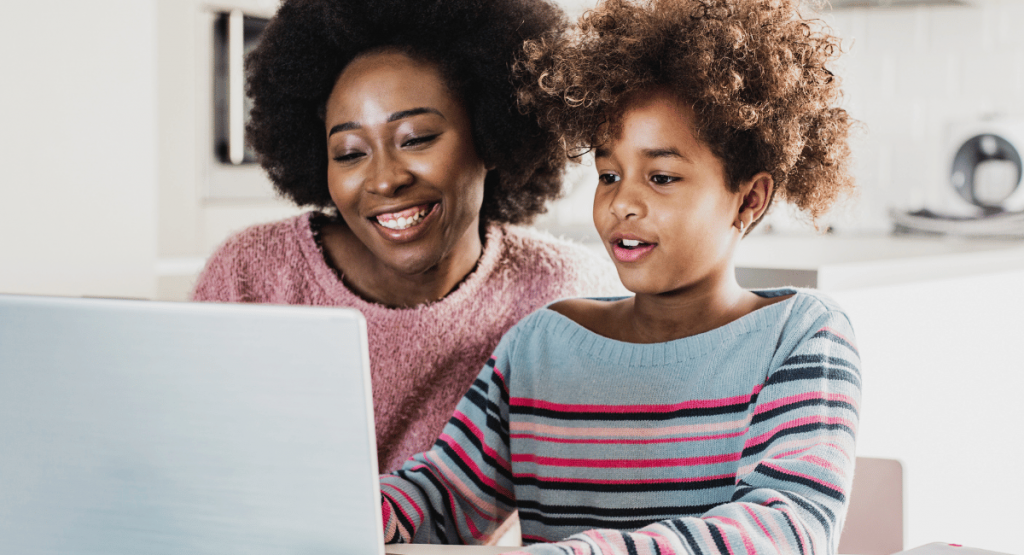 An African American woman with her young daughter smiling over the laptop learning together