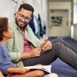 A teacher sits with his student in the hallway to provide one-on-one support, a reason teacher wellness is important.