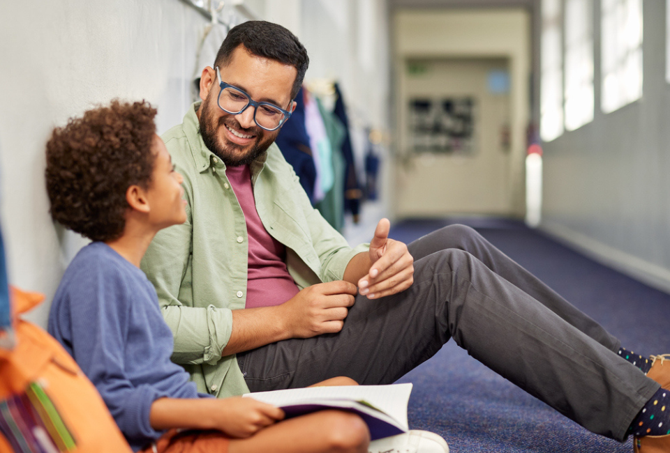 A teacher sits with his student in the hallway to provide one-on-one support, a reason teacher wellness is important.