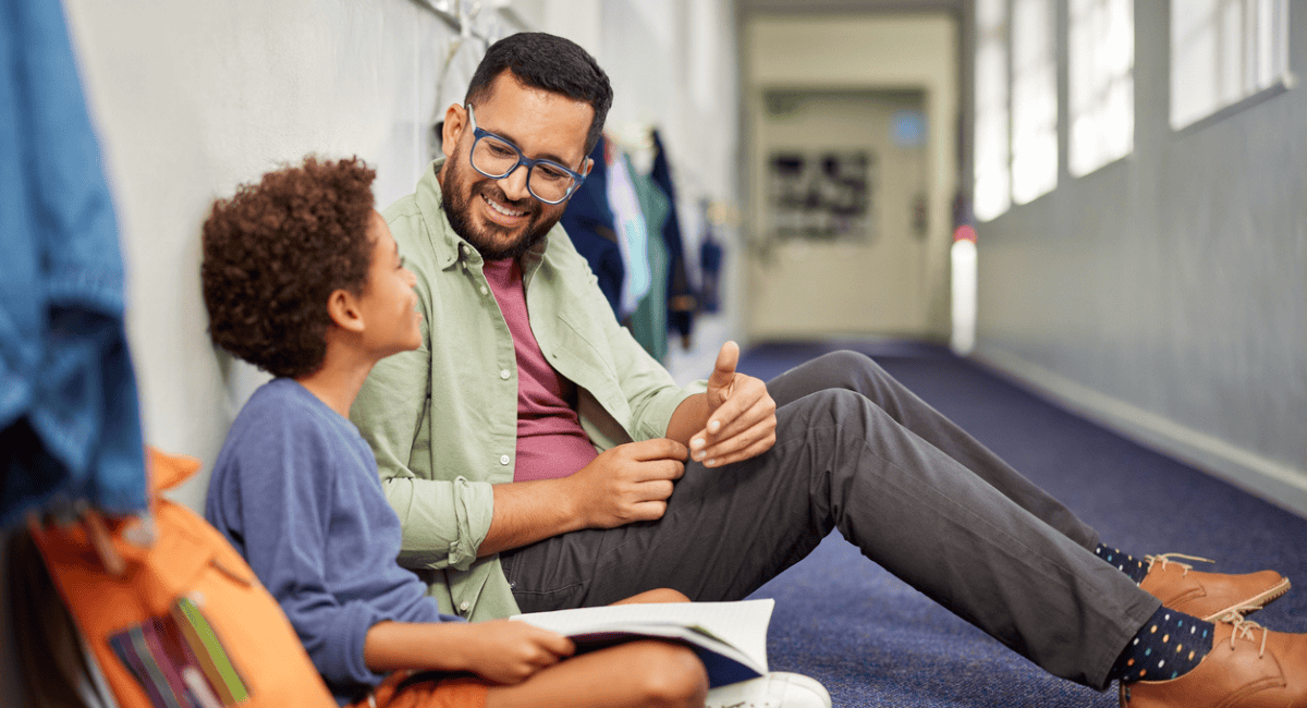 A teacher sits with his student in the hallway to provide one-on-one support, a reason teacher wellness is important.